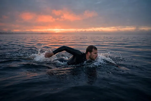 Triathlete in a wetsuit holding steady, controlled freestyle while pacing the swim leg of a triathlon at sunrise